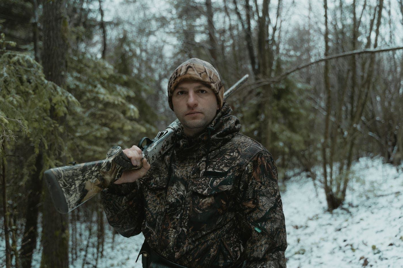 A hunter in camouflage holding a shotgun in a winter forest